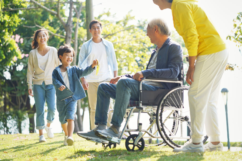 Family and caregiver with elderly person in wheelchair outdoors